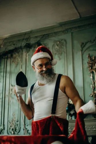 man in santa claus costume holding clothes iron