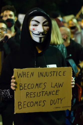person in an anonymous mask holding a banner on a protest